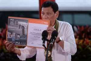 Philippine President Rodrigo Duterte holds up a certificate showing a Glock 30 handgun, awarded to him by a Philippine firearms importer for his fight against illegal drugs, during a "talk to the troops" visit in Manila on October 4, 2016. Rodrigo Duterte launched a fresh tirade at the United States on October 4, telling Barack Obama to "go to hell" as the longtime allies launched war games that the firebrand Philippine leader warned could be their last. / AFP PHOTO / TED ALJIBE